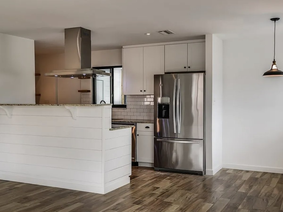 The renovated kitchen with white cabinets, granite counters, a subway tile backsplash, island hood and stainless refrigerator.