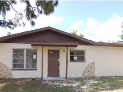 Single-story ranch in Bonita Springs, Florida, before renovation, with brown fascia and trim, a brown front door and stone facing beside the windows.
