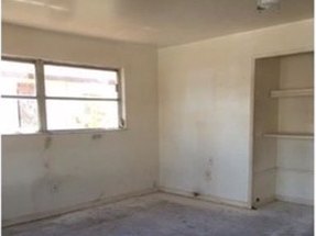 A bedroom before renovation, stripped to bare walls with the original closet shelving in place.