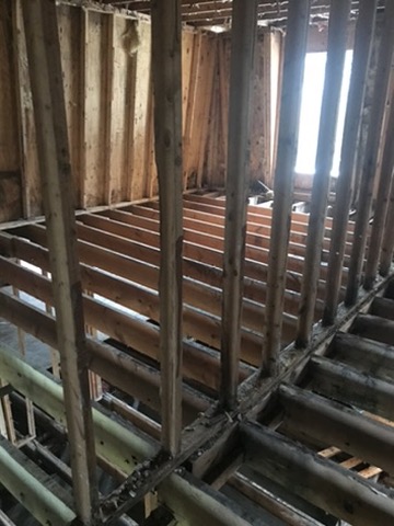 Floor joists with the subfloor removed, blackened along their full length, seen between exposed wall studs.