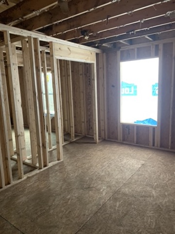 New light-colored stud walls and door openings framed beneath the original darkened ceiling joists, over a new subfloor.