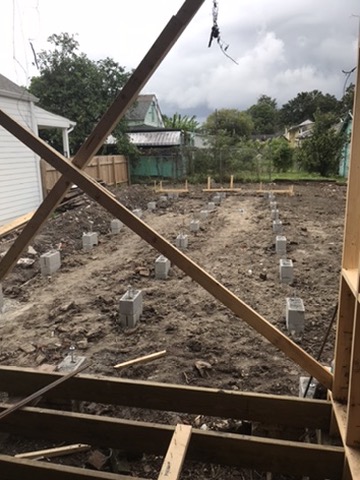 A grid of new concrete block piers laid out across bare ground where the rear of the house had stood.