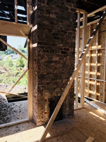 The original brick chimney standing full height inside new stud framing, with the roof open to the sky above it.