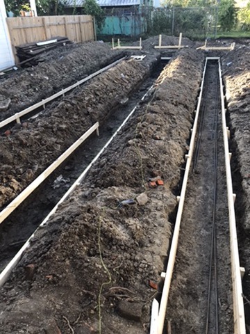 Excavated trenches across the rear of the site with timber formwork boards and reinforcing steel set in them.