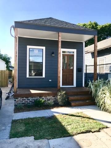 The finished front elevation: dark siding, a covered porch on timber posts, new front door and windows, standing on the original brick piers.