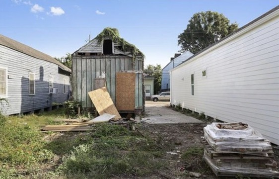 The rear of the house at purchase, seen from the back yard: ivy over the roof, plywood over the openings, and bare ground where the rest of the building had been.