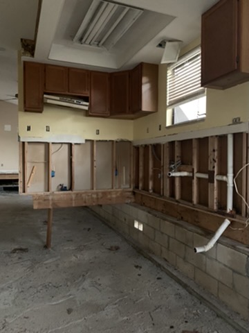 The kitchen in the same state: upper cabinets still hanging on the wall above stripped framing, block courses and open ground where the floor had been.