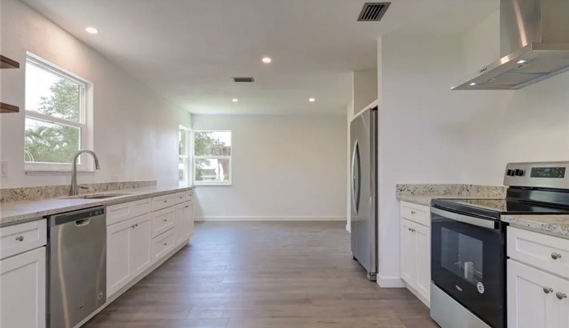 The completed kitchen: granite counters, white cabinetry, stainless appliances and a wall hood, open through to the living space.