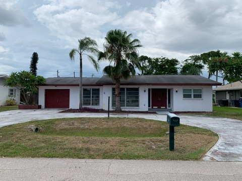 The house at purchase: a low ranch with a red garage door and red front door, palms in the lawn, seen from the street across a circular drive.
