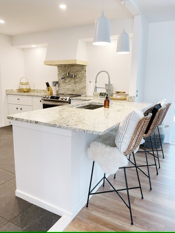 The completed kitchen: granite counters, white cabinetry, a stone backsplash and a peninsula with stools.