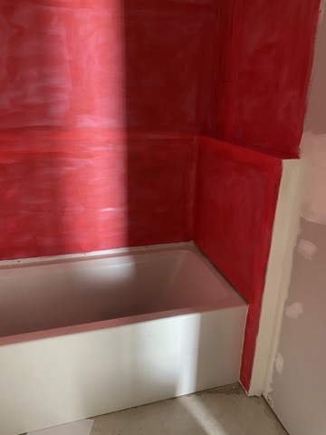 Red liquid waterproofing membrane rolled over the whole tub surround, up the walls and into the corners, before any tile went on.